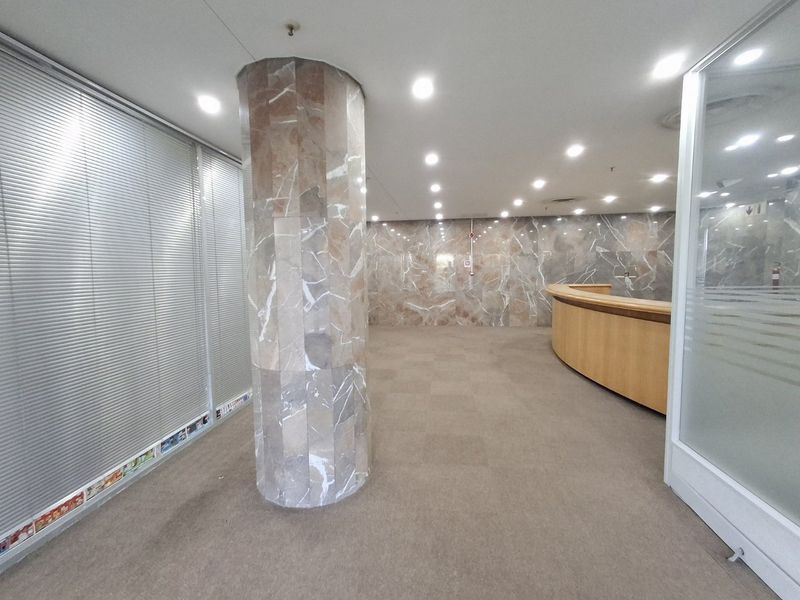 Spacious commercial entrance lobby featuring marble wall cladding, a central marble-clad column, recessed lighting, and a built-in reception desk.