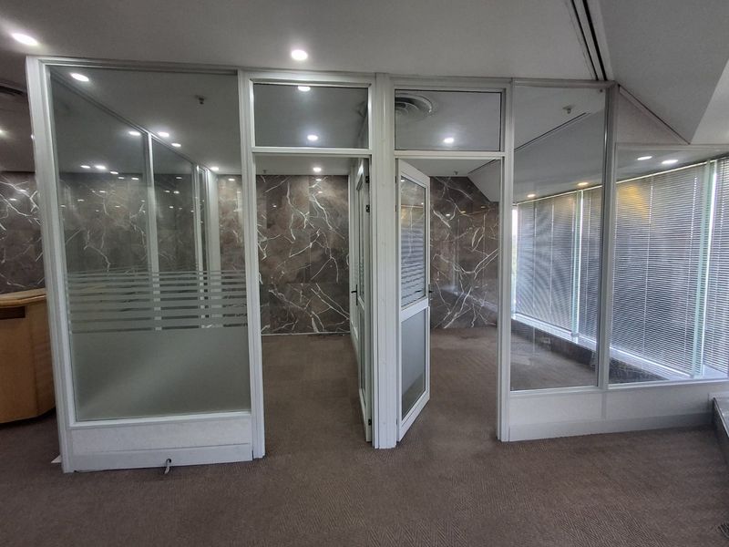 Modern commercial office space featuring glass partitions, marble-look wall finishes, recessed lighting, and carpeted flooring, providing a professional and clean work environment.