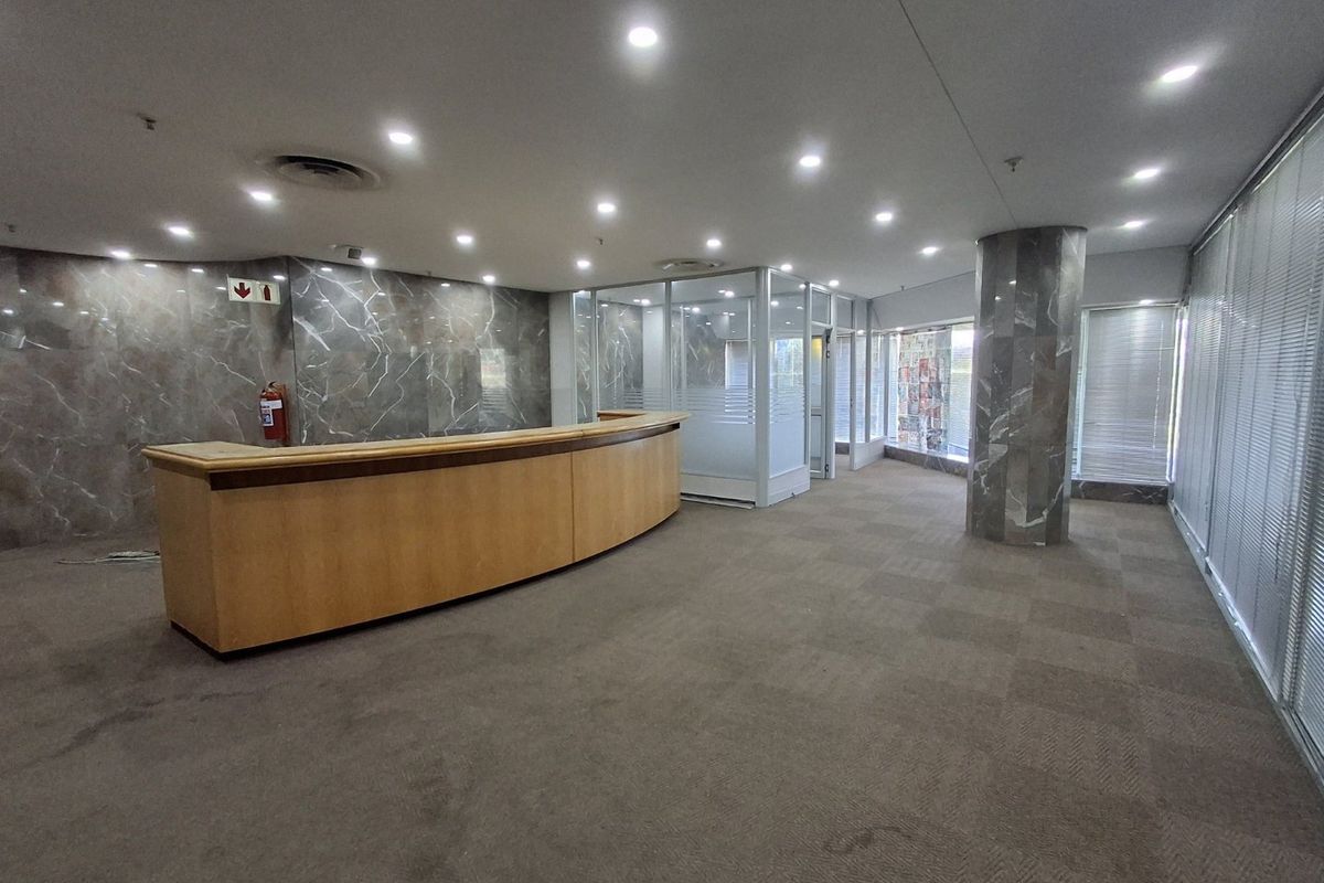 Spacious commercial reception area featuring a built-in desk, marble wall accents, glass-partitioned office space, and recessed ceiling lighting.