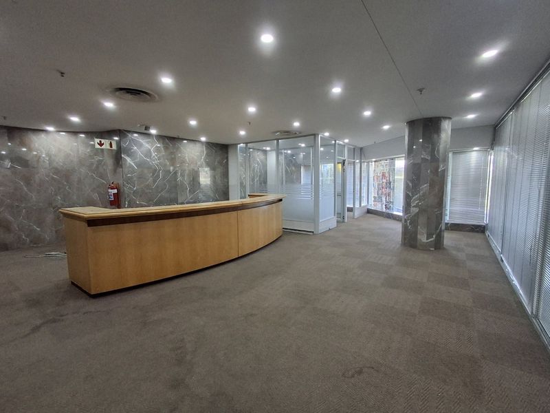 Spacious commercial reception area featuring a built-in desk, marble wall accents, glass-partitioned office space, and recessed ceiling lighting.