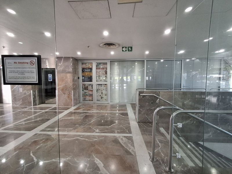 A professional commercial building lobby featuring polished marble flooring, marble wall cladding, glass partitions, and stainless steel handrails leading to an elevator.