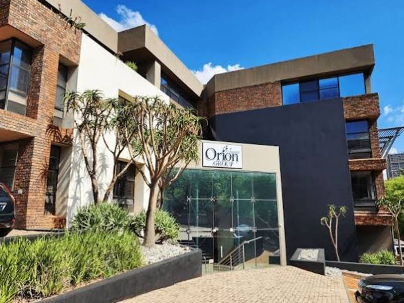 Modern commercial office building facade featuring a combination of brickwork, dark accents, and a prominent glass entrance.