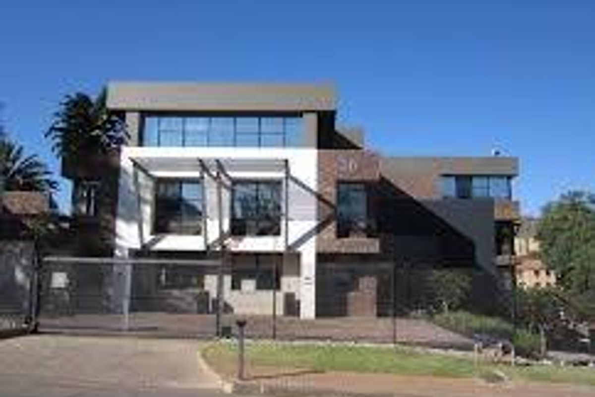 A modern commercial building facade featuring large glass windows, a paved driveway, and a secure metal gate entrance.