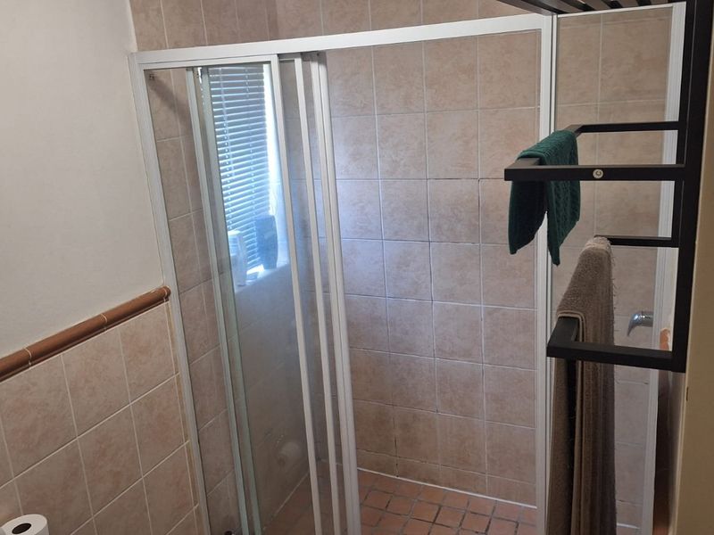 A functional bathroom featuring a shower enclosure with tiled walls and flooring, providing a practical space with standard fixtures.