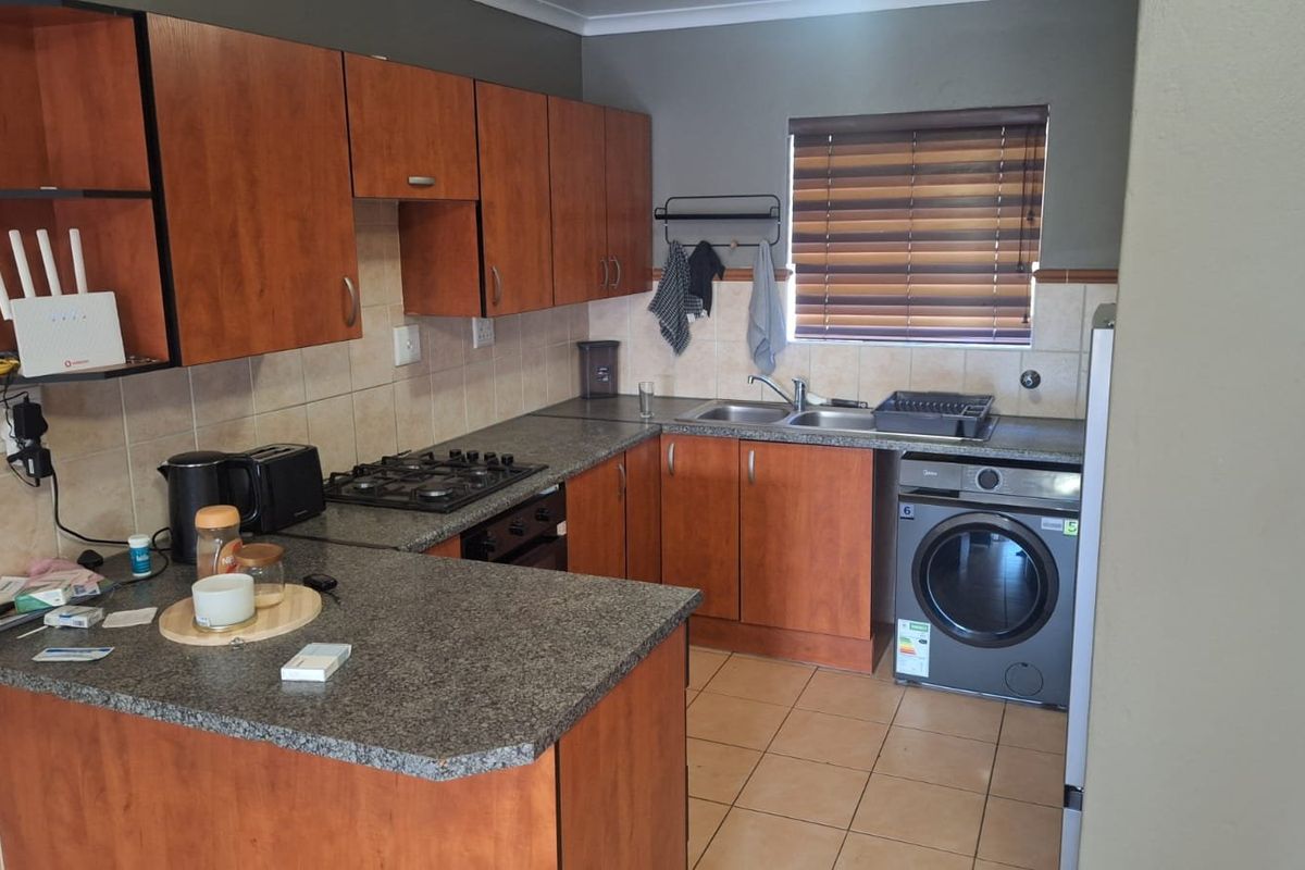 Functional kitchen featuring wood-finish cabinetry, granite-look laminate countertops, a gas hob, built-in oven, and integrated laundry appliance space.