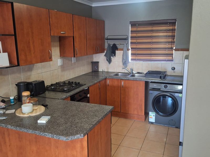 Functional kitchen featuring wood-finish cabinetry, granite-look laminate countertops, a gas hob, built-in oven, and integrated laundry appliance space.