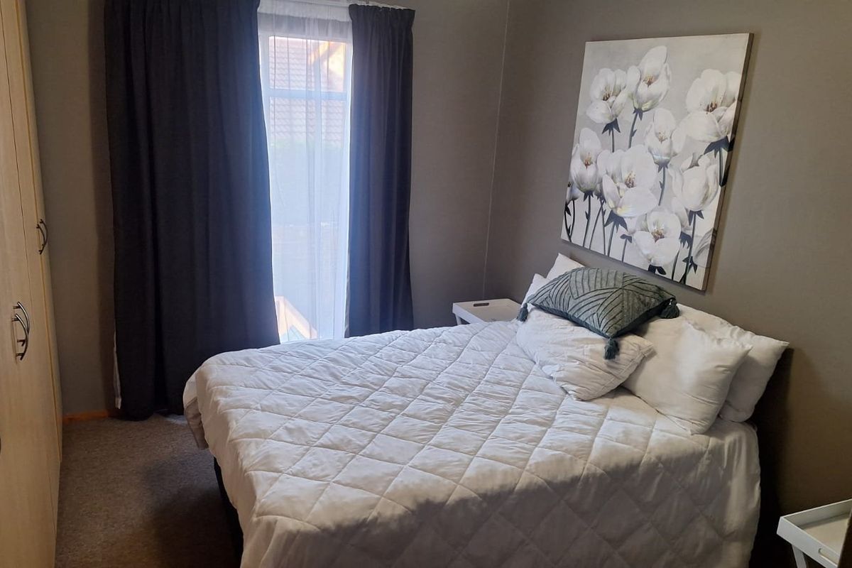 A cozy bedroom featuring neutral wall tones, carpeted flooring, and a functional built-in wardrobe with ample storage space.