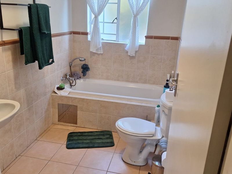 A functional bathroom featuring a pedestal basin, a built-in bathtub with a shower mixer, and a standard toilet with neutral wall and floor tiling.