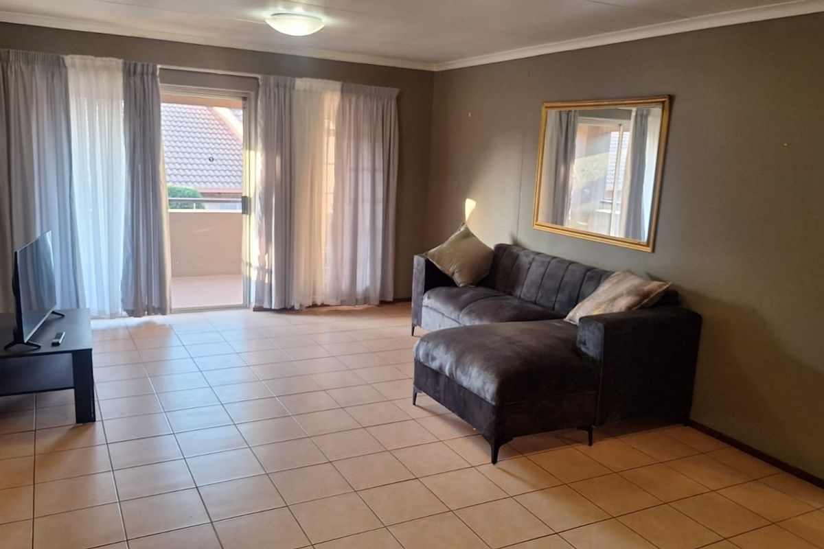 A spacious living room featuring neutral tiled flooring and a sliding glass door providing access to an outdoor balcony area.