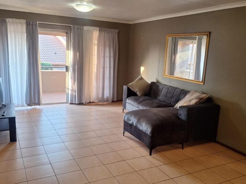 A spacious living room featuring neutral tiled flooring and a sliding glass door providing access to an outdoor balcony area.