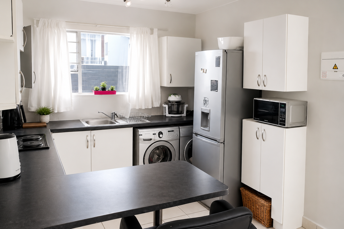 A functional kitchen featuring white cabinetry, dark laminate countertops, integrated hob, and space for laundry appliances, offering a clean and practical layout.