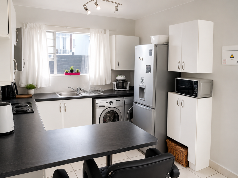 A functional kitchen featuring white cabinetry, dark laminate countertops, integrated hob, and space for laundry appliances, offering a clean and practical layout.