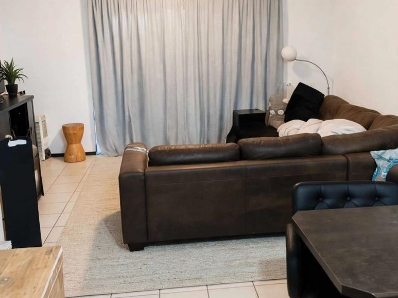 Open plan living area featuring neutral tiled flooring and a large window with curtain treatment, providing a functional and versatile space.