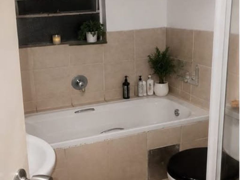 A compact bathroom featuring a bathtub with wall tiling and a toilet. The space requires minor repairs to the bathtub apron.