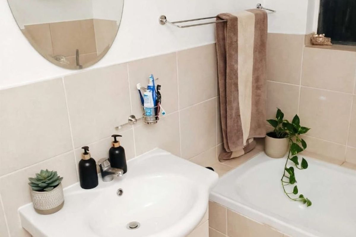 A functional bathroom featuring a vanity cabinet with a basin, a bathtub, and neutral wall tiling.