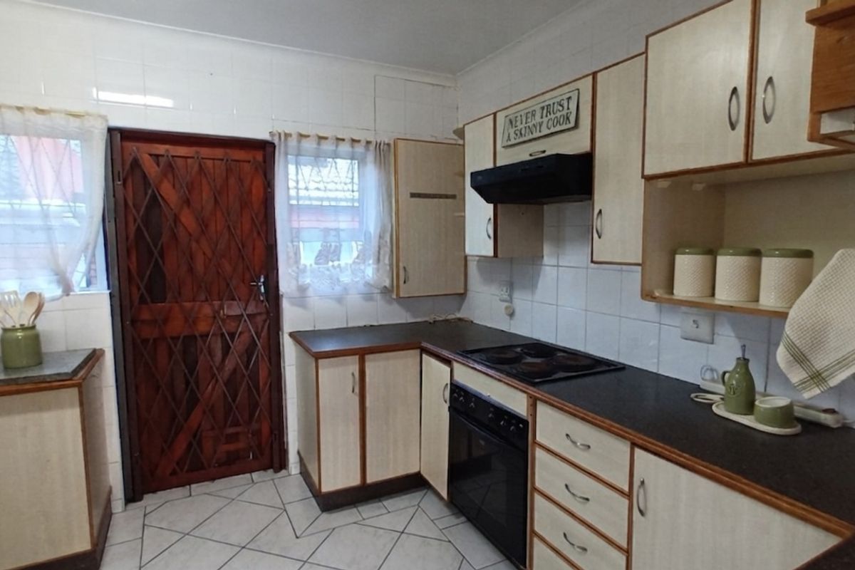 Functional kitchen featuring built-in cabinetry, laminate countertops, an electric hob, oven, extractor fan, and tiled splashbacks with a secure exterior door.