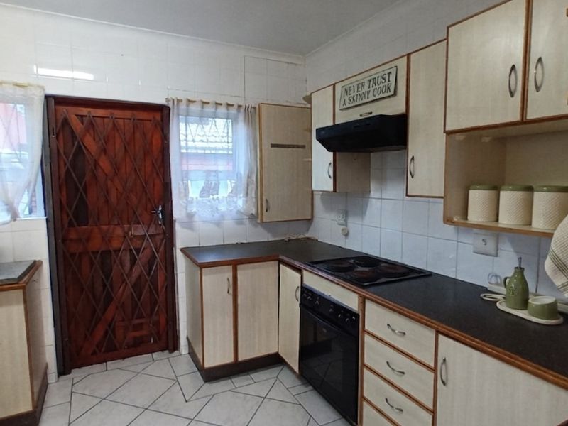 Functional kitchen featuring built-in cabinetry, laminate countertops, an electric hob, oven, extractor fan, and tiled splashbacks with a secure exterior door.
