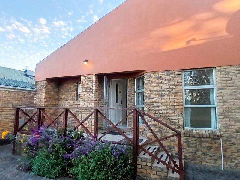 Front entrance of a face brick house featuring a timber balustrade, security gate, and paved walkway access.