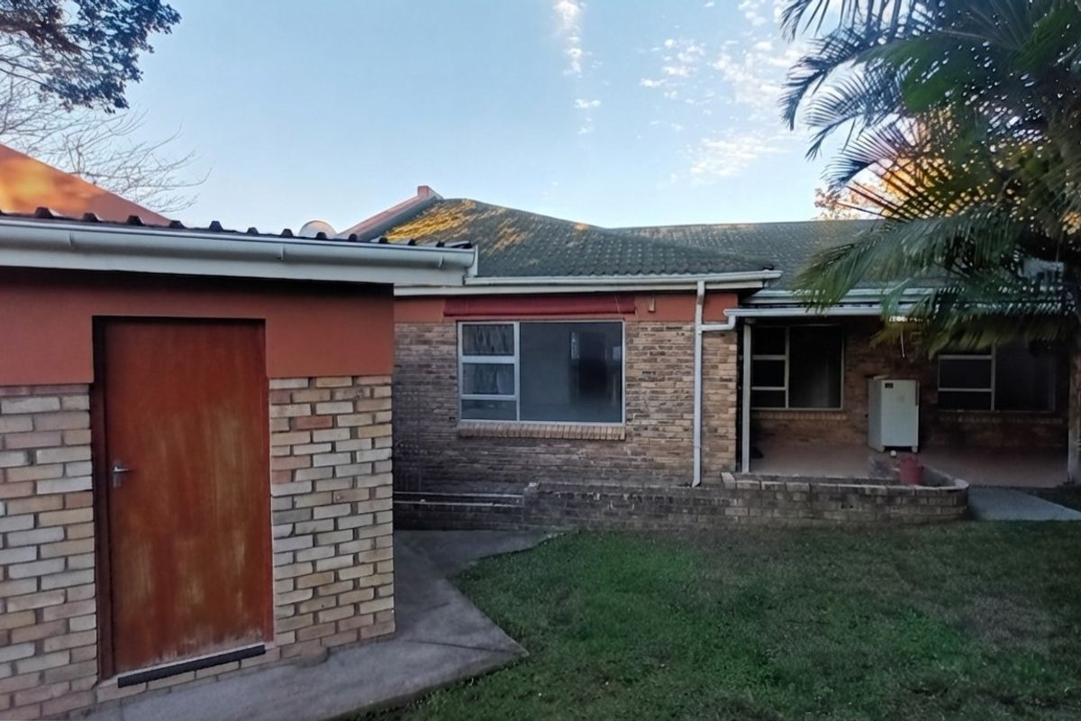 Rear view of the property featuring a brick facade, tiled roof, and a small concrete patio area adjacent to the garden.