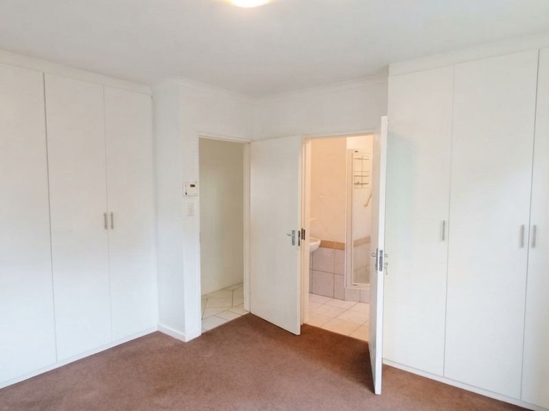 A clean, empty bedroom featuring extensive built-in cupboard storage, neutral finishes, and direct access to an adjoining en-suite bathroom.