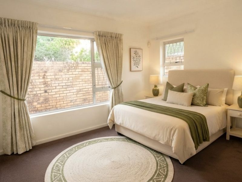 A well-maintained bedroom featuring neutral tones, carpeted flooring, built-in wardrobe storage, and large windows allowing for natural light.