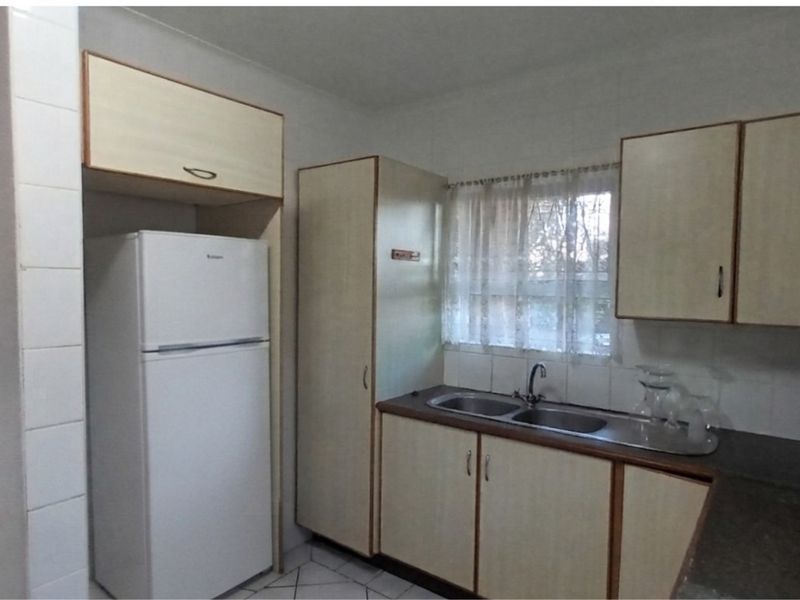 A functional kitchen featuring laminate cabinetry, a double bowl stainless steel sink, tiled splashbacks, and tiled flooring.