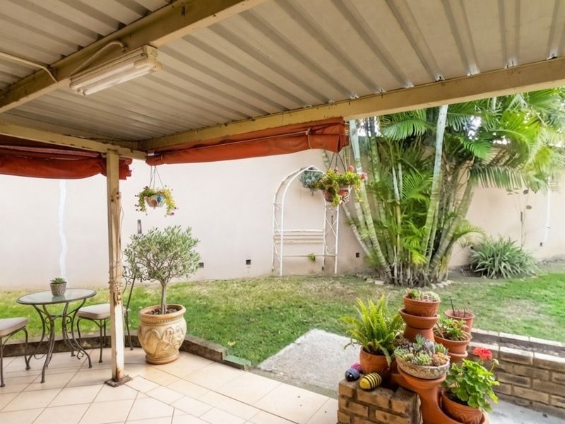 A covered patio area featuring tiled flooring, a corrugated metal roof, and a brick retaining wall overlooking a private garden space.