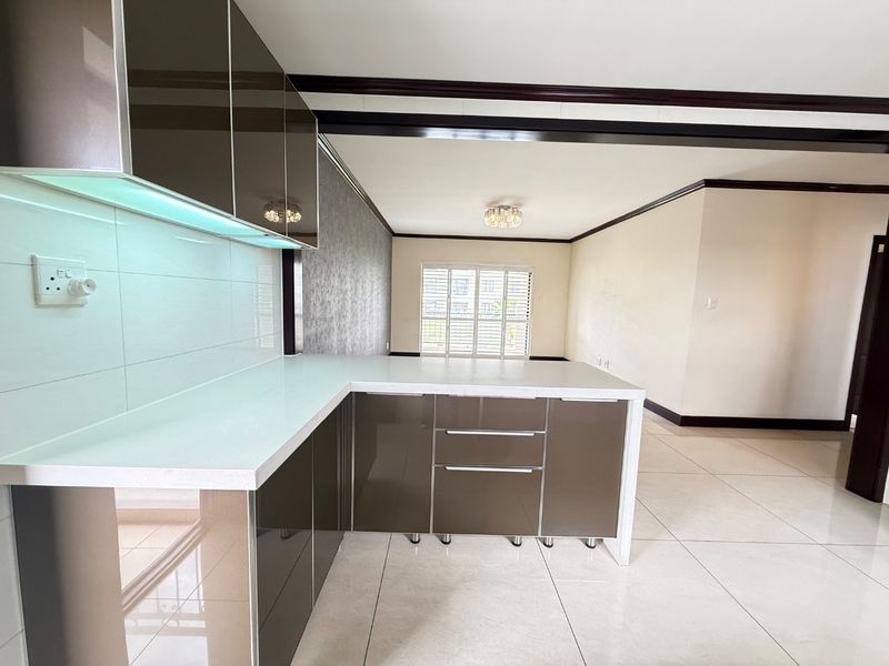 Modern open-plan kitchen and living area featuring sleek glossy cabinetry, stone countertops, tiled flooring, and elegant ceiling detailing.
