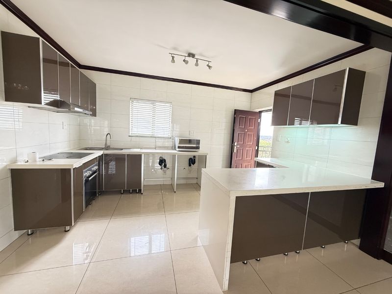 Modern kitchen featuring high-gloss cabinetry, stone countertops, integrated oven and hob, and tiled finishes throughout.