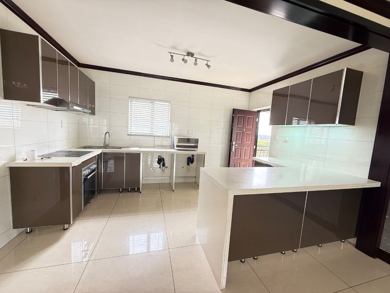 Modern kitchen featuring glossy cabinetry, stone countertops, built-in oven, electric hob, and tiled finishes throughout, offering a clean and functional workspace.