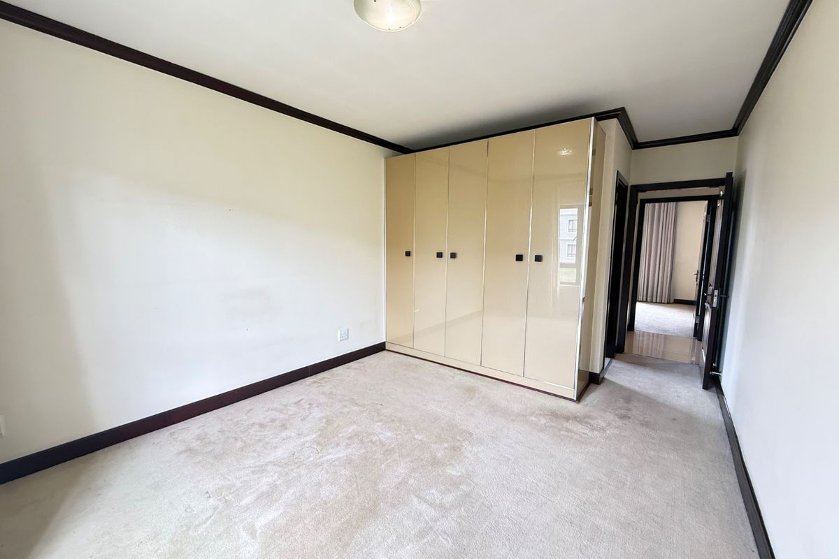 A vacant bedroom featuring neutral carpeted flooring, dark trim detailing, and high-gloss built-in cupboards providing ample storage space.