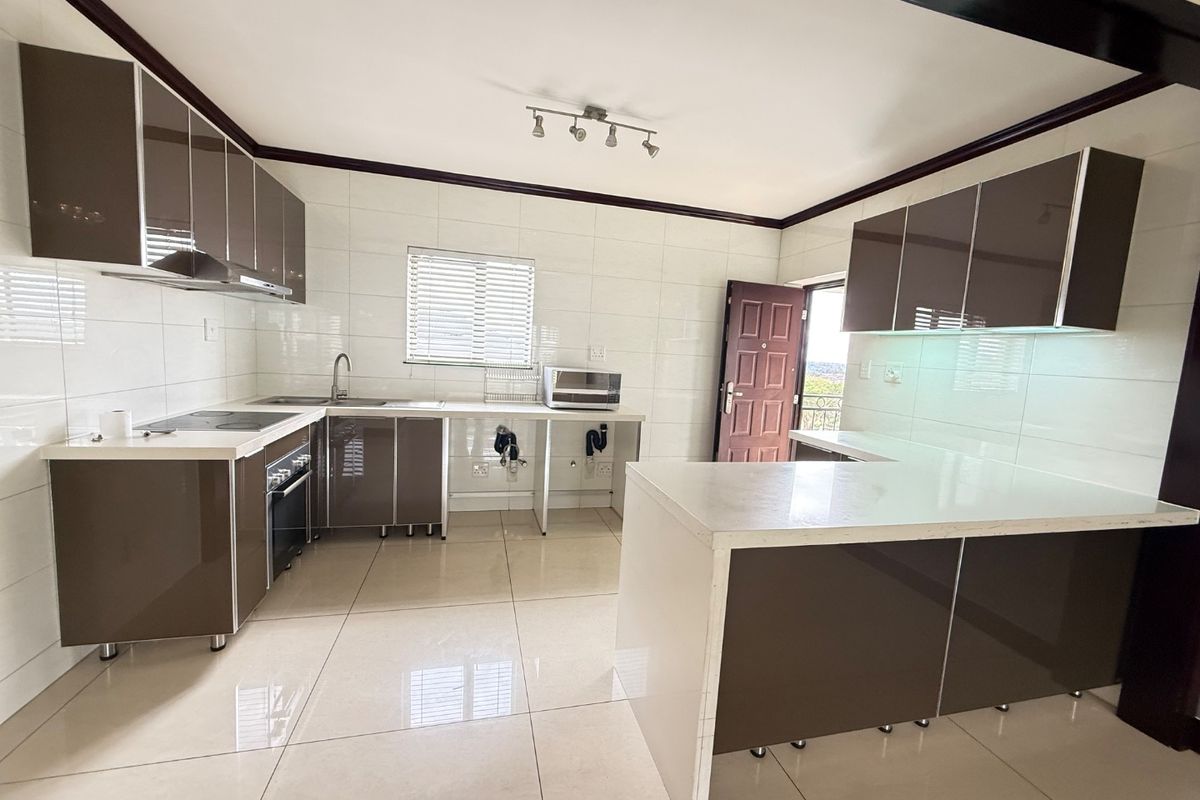 Modern kitchen featuring glossy brown cabinetry, stone countertops, built-in oven, electric hob, and tiled finishes throughout in an open-plan layout.