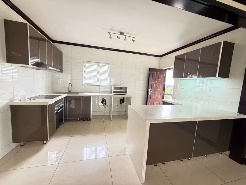 Modern kitchen featuring glossy brown cabinetry, stone countertops, built-in oven, electric hob, and tiled finishes throughout in an open-plan layout.