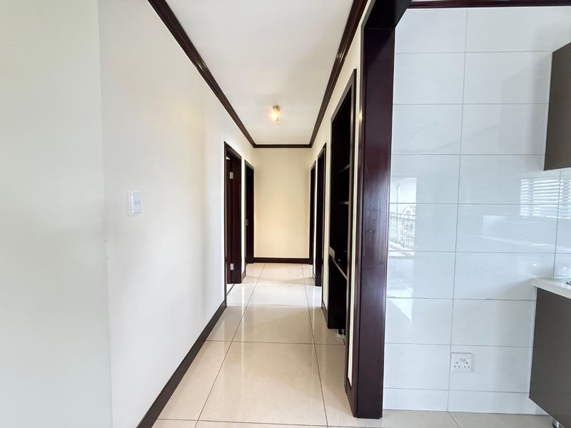A clean, well-maintained hallway featuring neutral tiled flooring, dark wood door frames, and crown molding, providing access to multiple rooms.