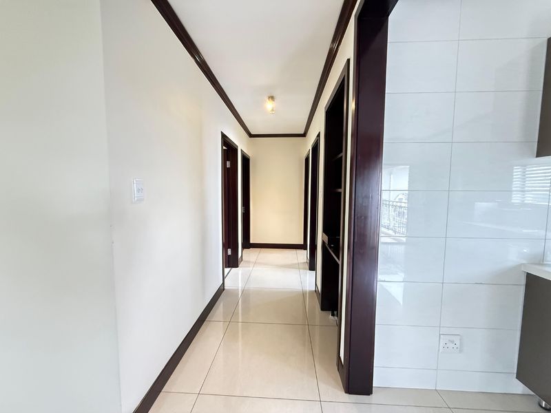 A clean, well-maintained hallway featuring neutral tiled flooring, dark wood trim, and multiple doorways leading to other rooms in the apartment.