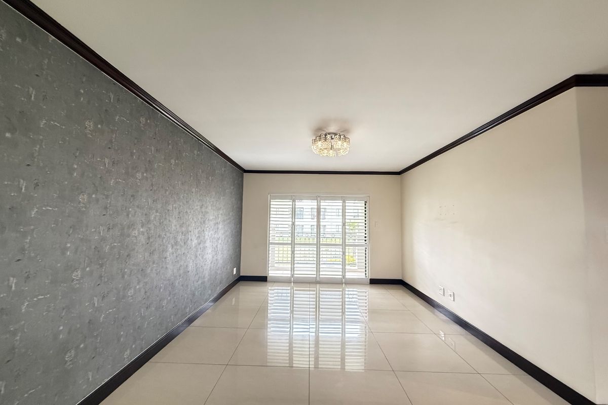 A spacious, empty living area featuring polished tiled floors, a textured feature wall, and sliding glass doors with security shutters leading to the exterior.