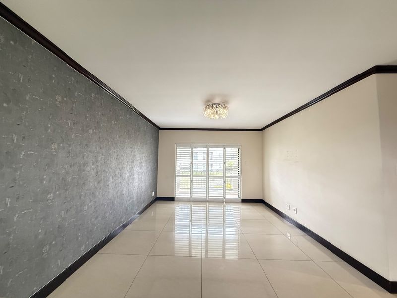 A spacious, empty living area featuring polished tiled floors, a textured feature wall, and sliding glass doors with security shutters leading to the exterior.