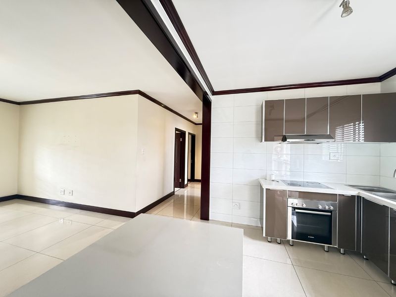 Open-plan living area featuring a modern kitchen with built-in cabinetry, electric hob, oven, and extractor fan, finished with neutral tiled flooring throughout.