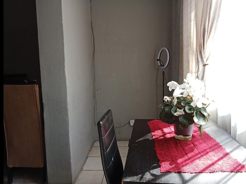A dining area featuring tiled flooring and natural light from a window, currently showing signs of wear and exposed wall wiring.