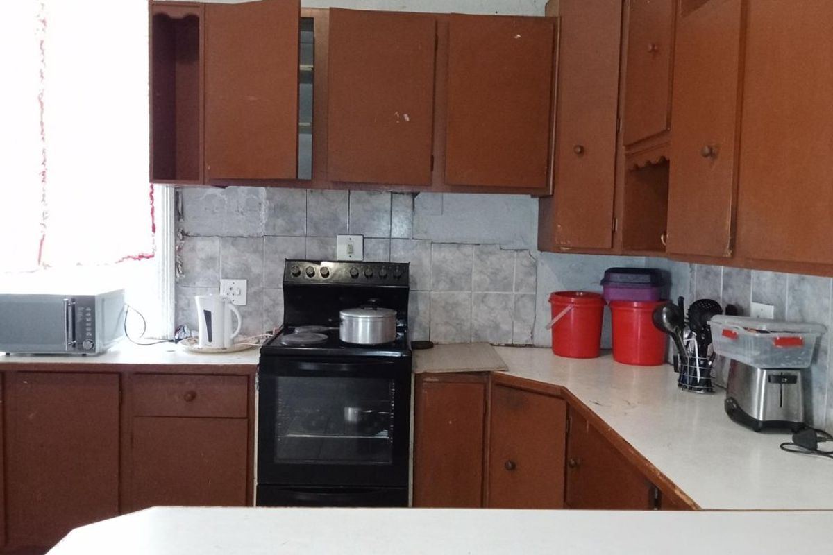 A dated kitchen featuring brown built-in cabinetry, a tiled backsplash, and a freestanding stove, requiring modernization and cosmetic updates.