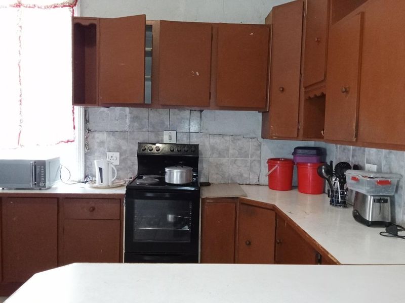 A dated kitchen featuring brown built-in cabinetry, a tiled backsplash, and a freestanding stove, requiring modernization and cosmetic updates.