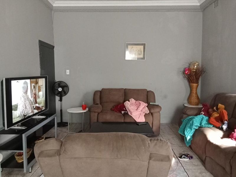 A living room featuring tiled flooring and coved ceiling cornices, currently requiring cosmetic updates to the wall finishes.