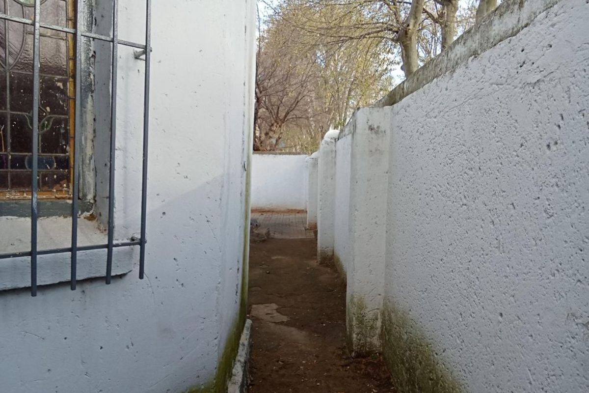 A narrow side passage between the house exterior and a high boundary wall, showing signs of weathering and damp at the base.