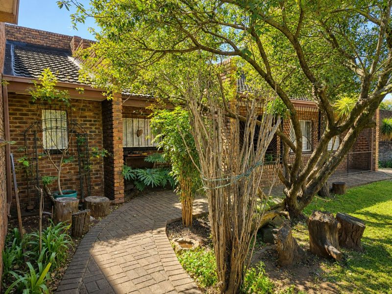 A view of the rear exterior featuring a face brick facade, tiled roof, and a paved walkway leading through a landscaped garden area.