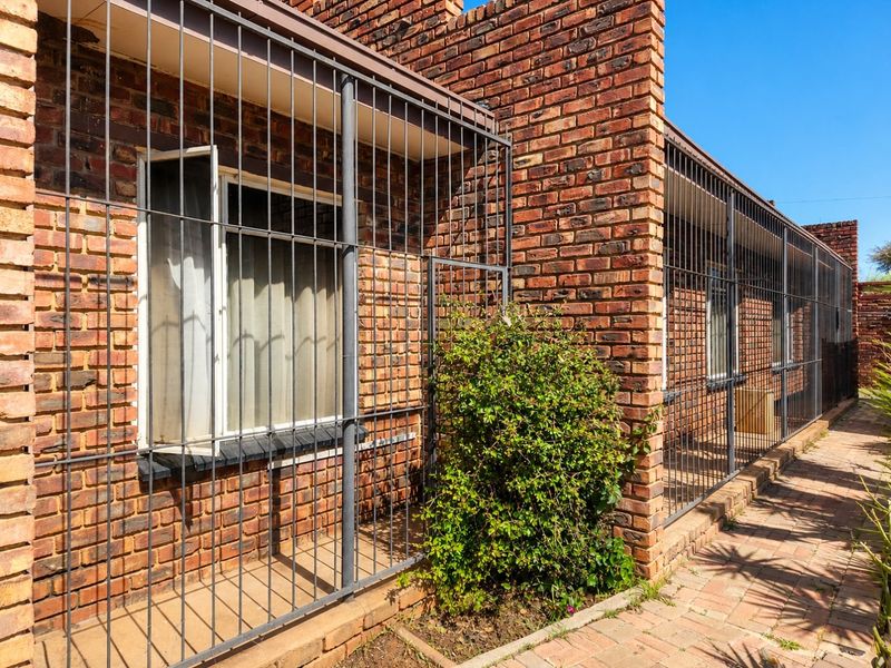 A view of the rear exterior featuring face brick walls, security bars over the windows, and a paved walkway.