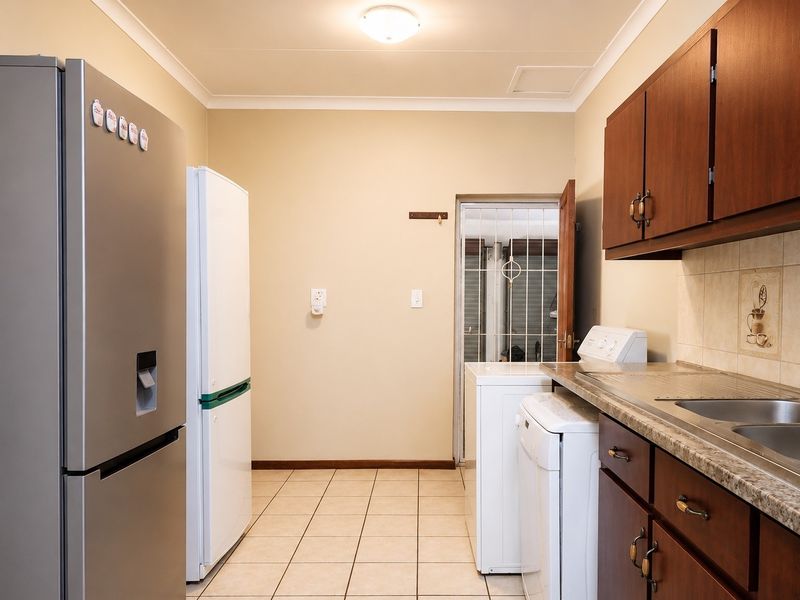 A functional laundry room featuring built-in wooden cabinetry, laminate countertops, a stainless steel sink, and tiled flooring with direct access to an exterior security gate.