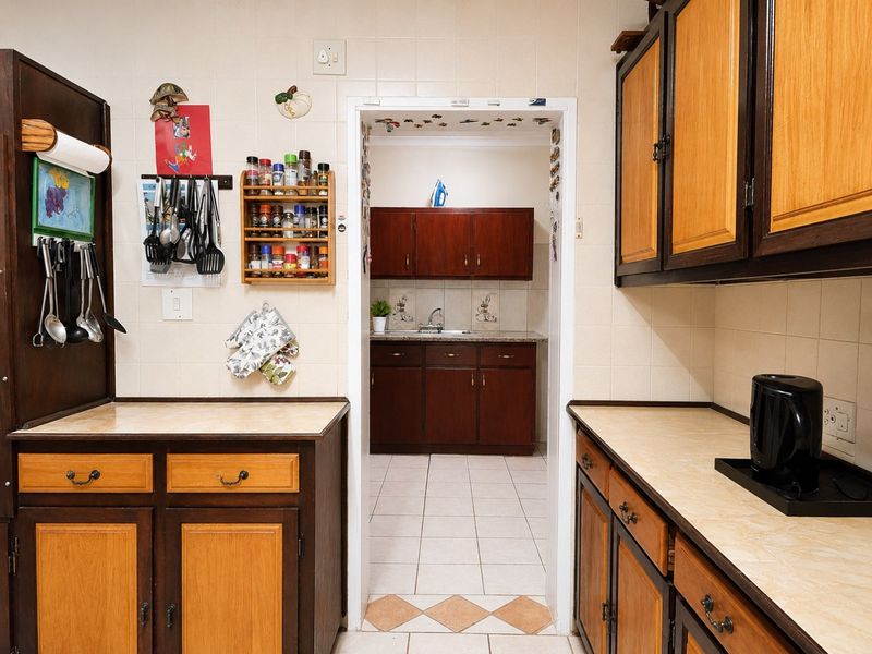A functional kitchen featuring traditional wood-toned cabinetry, laminate countertops, and a tiled backsplash, with an adjoining scullery area visible through the doorway.