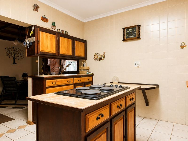 A functional kitchen featuring wooden cabinetry, a central island with an integrated electric hob, and tiled wall finishes.