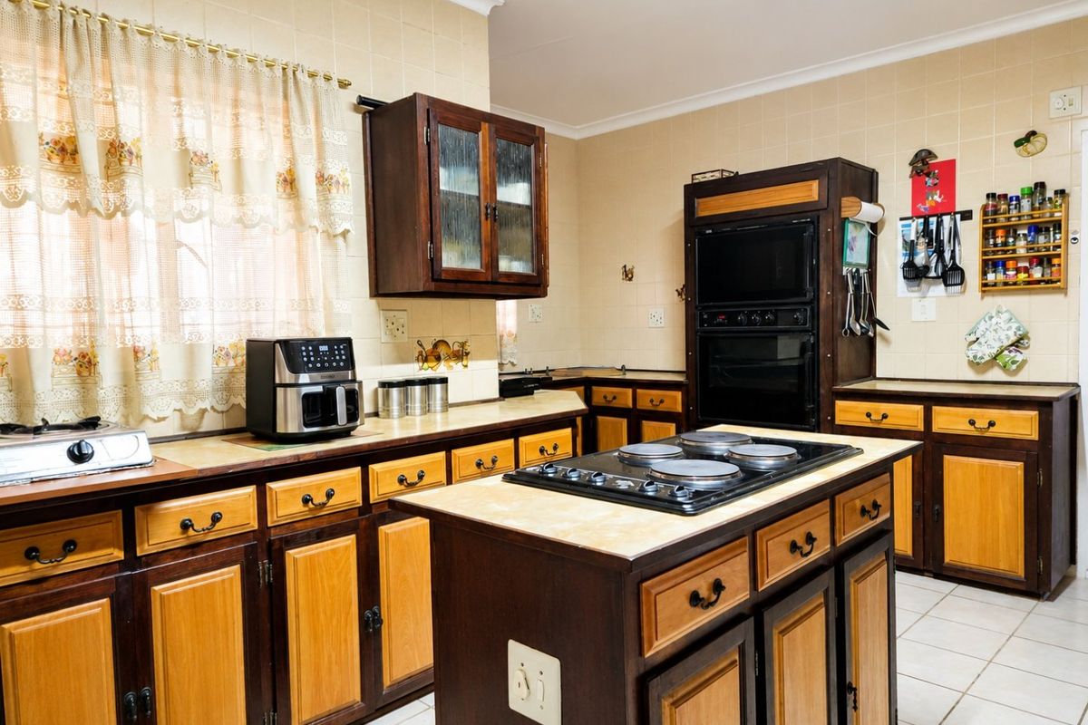 A traditional kitchen featuring two-tone wooden cabinetry, a central island with an integrated electric hob, built-in oven, and tiled backsplash.