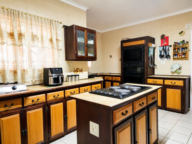A traditional kitchen featuring two-tone wooden cabinetry, a central island with an integrated electric hob, built-in oven, and tiled backsplash.